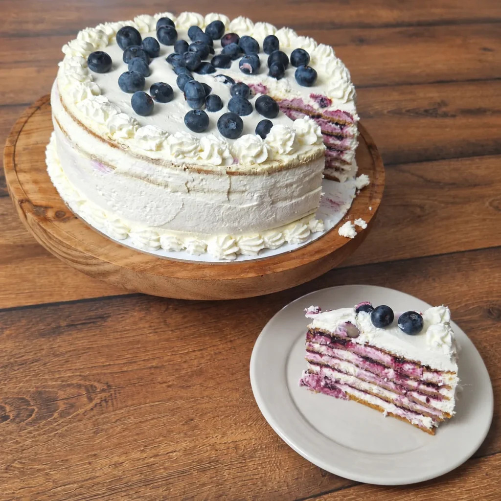 Medovik torta sa borovnicama i isečeno parče sa slojevima bele kreme i fila od borovnica