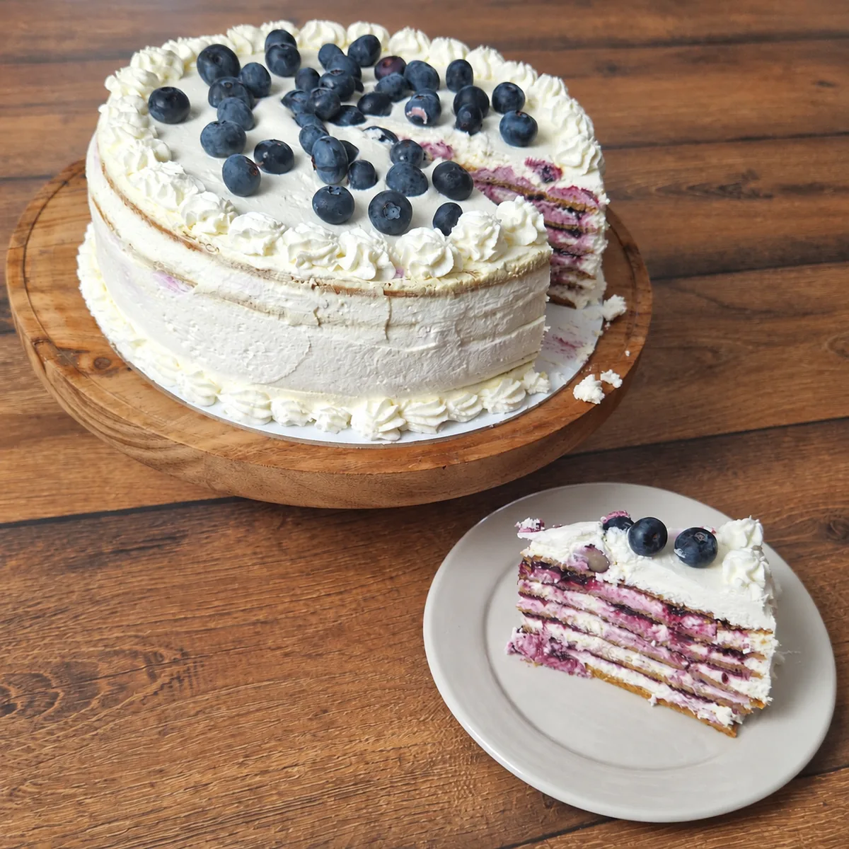 Medovik torta sa borovnicama i isečeno parče sa slojevima bele kreme i fila od borovnica